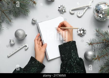 Donna che scrive piani per 2025 anni in notebook e decorazioni natalizie su sfondo chiaro Foto Stock