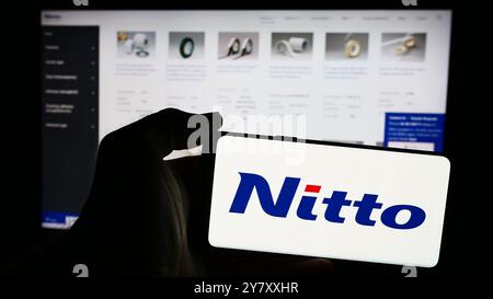 In questa immagine, una persona ha in mano uno smartphone con il logo dell'azienda chimica giapponese Nitto Denko Corporation davanti al suo sito web. Foto Stock