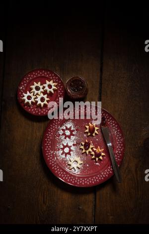 Biscotti di Natale (Spitzbuben) con marmellata, coltello e su piatti rossi, su fondo di legno Foto Stock