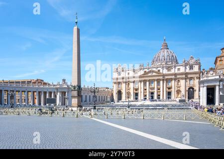 I visitatori passeggiano attraverso Piazza San Pietro in una giornata luminosa, ammirando la magnifica basilica di San Pietro e l'imponente obelisco contro un cielo azzurro. Foto Stock