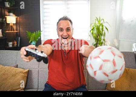 Uomo di mezza età eccitato che gioca ai videogiochi a casa Foto Stock