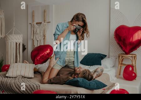 Una giovane donna che fotografa il suo ragazzo con una macchina fotografica rétro mentre si rilassa a letto a casa insieme Foto Stock