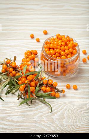 Bacche di spinoso marino in un bicchiere accanto ai ramoscelli con foglie Foto Stock