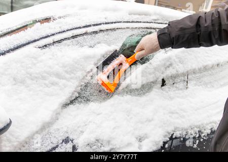 Guida nella stagione invernale. Primo piano di una mano che pulisce il parabrezza del veicolo da ghiaccio e neve. Trasporto, inverno, meteo, persone e veicoli Foto Stock