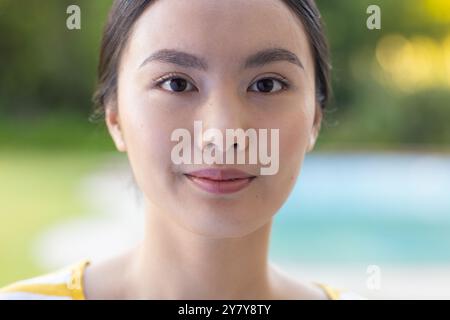 Sorridente giovane donna asiatica con trucco naturale che posa all'aperto, godendo di una giornata di sole Foto Stock