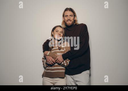 Giovane coppia alla moda che abbraccia e guarda la macchina fotografica con sorrisi su sfondo beige Foto Stock