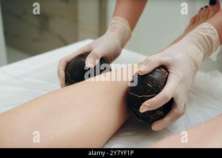 Il massaggiatore utilizza pietre vulcaniche per un trattamento rilassante sulle gambe Foto Stock