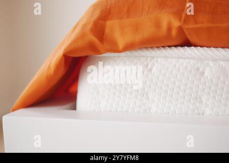 Un comodo letto con materasso bianco adornato con accenti di arancione brillante Foto Stock