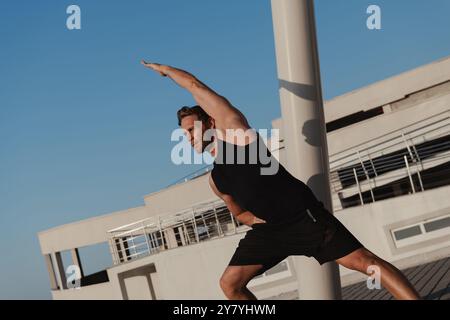 Uomo muscolare confidente in abbigliamento sportivo che fa esercizi di stretching all'aperto la mattina presto Foto Stock