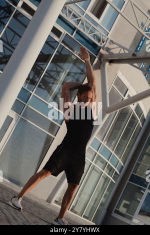 Bel muscoloso in abbigliamento sportivo che fa esercizi di stretching all'aperto la mattina presto Foto Stock