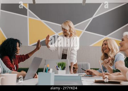 Due donne mature che danno alti voti durante una riunione di lavoro di gruppo in ufficio Foto Stock