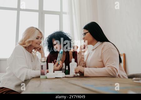 Tre donne mature che esaminano i prodotti di bellezza sedute alla scrivania insieme Foto Stock