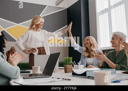 Due donne mature felici che danno soldi alti mentre hanno una riunione di lavoro di gruppo in ufficio Foto Stock