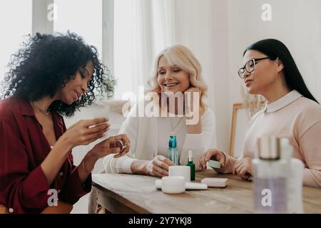 Tre donne mature che esaminano i prodotti di bellezza sedute alla scrivania insieme Foto Stock