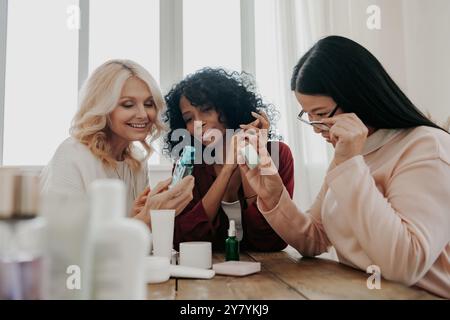 Tre donne mature che esaminano i prodotti di bellezza sedute alla scrivania insieme Foto Stock