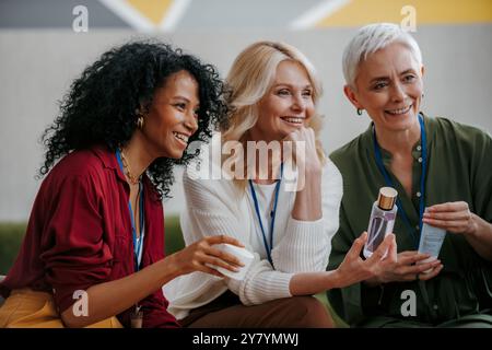 Tre donne mature felici che esaminano prodotti di bellezza durante una conferenza specializzata Foto Stock