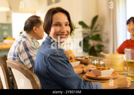 A casa, una donna sorridente di mezza età che gusta un pasto con la famiglia al tavolo da pranzo, condividendo momenti felici Foto Stock