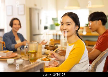 A casa, mangiando insieme, la famiglia asiatica si gusta il pasto e sorride al tavolo da pranzo Foto Stock