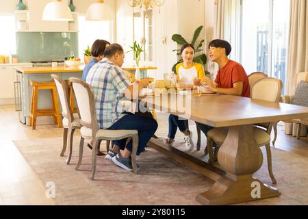 A casa, la famiglia asiatica si siede al tavolo da pranzo, si fa colazione e si chiacchiera insieme Foto Stock