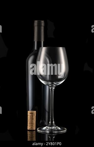 Una bottiglia chiusa di vino rosso con un bicchiere e un banco di sughero davanti a uno sfondo nero Foto Stock
