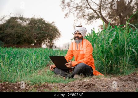 Agricoltore rurale indiano che lavora su un computer portatile nel campo delle colture Foto Stock