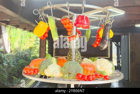 Una colorata disposizione sospesa di vari tipi di frutta e verdura, tra cui banane, arance, patate, cetrioli, e altro ancora, sotto una tettoia Foto Stock