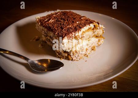 Fetta di tiramisù italiano a base di caffè, cioccolato, mascarpone, pan di Spagna e panna su un piatto con un cucchiaio Foto Stock