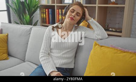 Una giovane donna rilassata ama la musica con le cuffie in un accogliente soggiorno con arredi eleganti Foto Stock