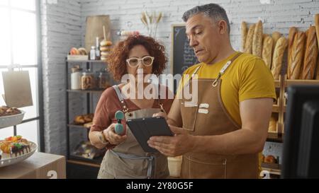 Uomini e donne che lavorano insieme in una panetteria, discutono su un tablet all'interno di un accogliente negozio con pane fresco e pasticcini Foto Stock