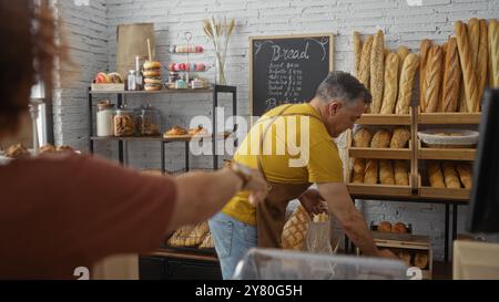 Uomo e donna nella sala da forno come lavoratore e cliente circondati da vari tipi di pane in esposizione Foto Stock