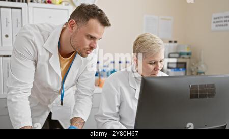 Un uomo e una donna, vestiti con camici da laboratorio, analizzano intensamente i dati su uno schermo di un computer in un moderno ambiente di laboratorio. Foto Stock