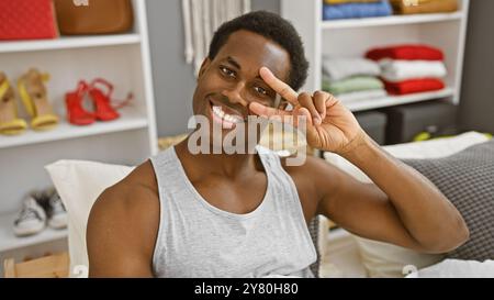 Un giovane afroamericano sorridente che posa giocosamente in una camera da letto informale al coperto. Foto Stock