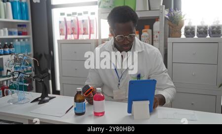 Bell'uomo che lavora in una farmacia con un lettore di codici a barre e un tablet con vari prodotti farmaceutici esposti sugli scaffali dietro h Foto Stock