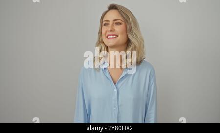 Il ritratto di una giovane donna bionda sorridente con una camicia blu su sfondo bianco trasuda bellezza e semplicità. Foto Stock