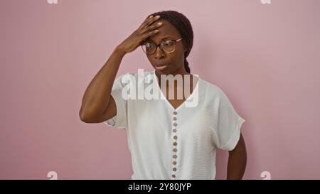 Donna afroamericana in piedi su uno sfondo rosa, indossa occhiali e una camicia bianca, che mostra un'espressione premurosa con una mano sul suo petto Foto Stock