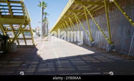 Vista sfocata del ponte urbano all'aperto che enfatizza la struttura in metallo giallo con attraversamento pedonale sfocato e palme sotto il cielo limpido Foto Stock