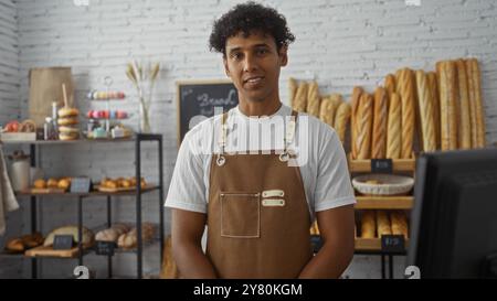 Bel giovane che lavora in una panetteria, sorridendo con vari tipi di pane in mostra dietro il bancone. Foto Stock