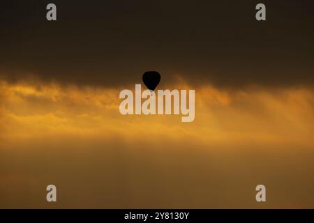 Silhouette di una mongolfiera che si solleva tra le nuvole del tramonto con deboli raggi solari che fuggono dalle nuvole. Foto Stock