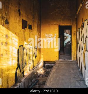 Interno della fabbrica abbandonato. Graffiti su pareti gialle all'interno di una pianta trascurata. Archeologia industriale. Foto Stock