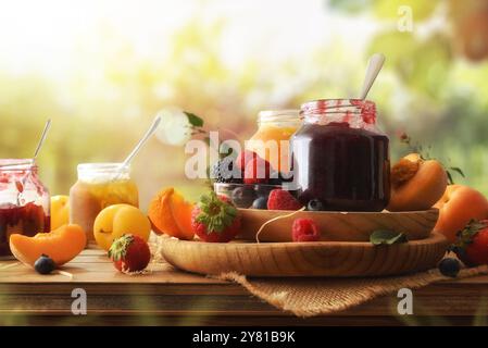 Diversi vasetti di marmellata di vari sapori con frutti diversi su una tavola rustica di legno con uno sfondo di colture in natura. Vista frontale. Foto Stock