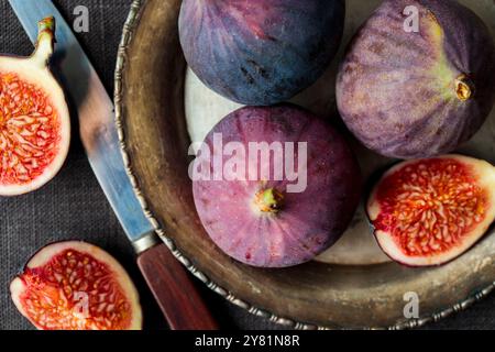 Fichi freschi su sfondo scuro, interi e affettati fichi maturi, deliziosi e dolci con un coltello da cucina su un vecchio piatto di metallo rustico, striscione orizzontale Foto Stock