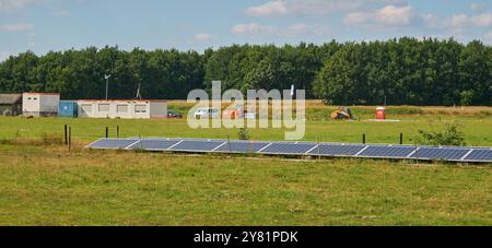 cantiere per una fattoria a energia solare alla luce del sole vicino a un'autostrada, con alberi e cieli blu. Impianto su piccola scala nel terreno. Foto Stock