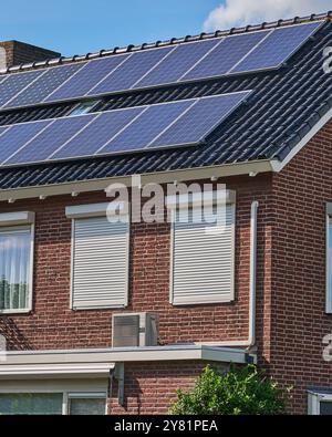 moderna unità pompa di calore a sorgente d'aria montata sulla parete esterna di una casa con pannelli solari sul tetto, a dimostrazione di una tecnologia a basso consumo energetico per Foto Stock