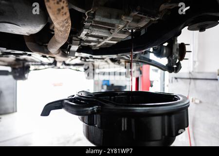 Una vista dettagliata di un cambio dell'olio in corso in un'officina di riparazione automobilistica. L'olio viene scaricato dal motore della vettura in una vaschetta di raccolta. Foto Stock