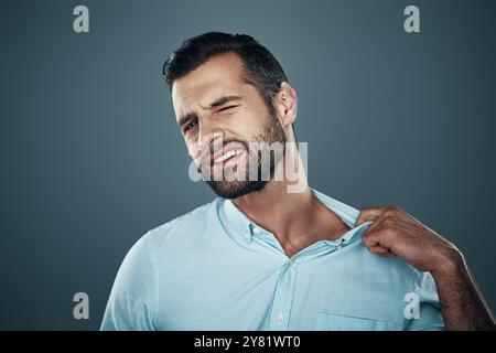 Scomodo. Giovane stanco che tira il collare mentre si sta in piedi su sfondo grigio Foto Stock