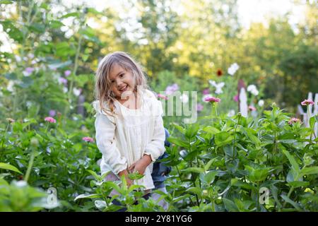 Sorridente ragazza in piedi tra lussureggianti piante verdi in un giardino con fiori che fioriscono sullo sfondo. Foto Stock