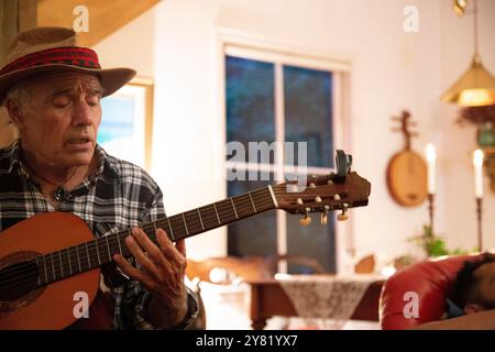 Uomo anziano che suona una chitarra acustica in un salotto illuminato di notte, Auckland, nuova Zelanda Foto Stock