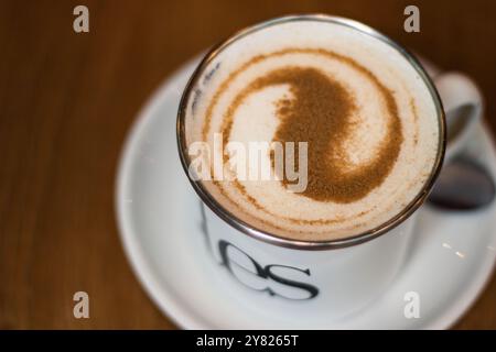 Tazza da caffè su un tavolo di legno con cannella sopra la schiuma su sfondo di legno Foto Stock