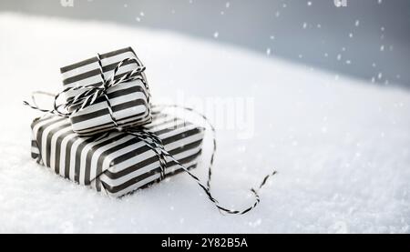 Regali di Natale, regali avvolti in carta bianca e nera a righe impilata sulla neve, legati con cordoncino, festività natalizie minimaliste, bokeh invernale Foto Stock