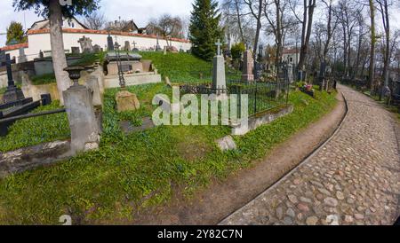 Un sentiero acciottolato che si snoda attraverso un vecchio cimitero con varie lapidi e recinzioni di ferro. Nella b sono visibili alberi senza foglie e fiori blu Foto Stock